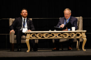 Two men sitting in chairs behind a table with a microphone.