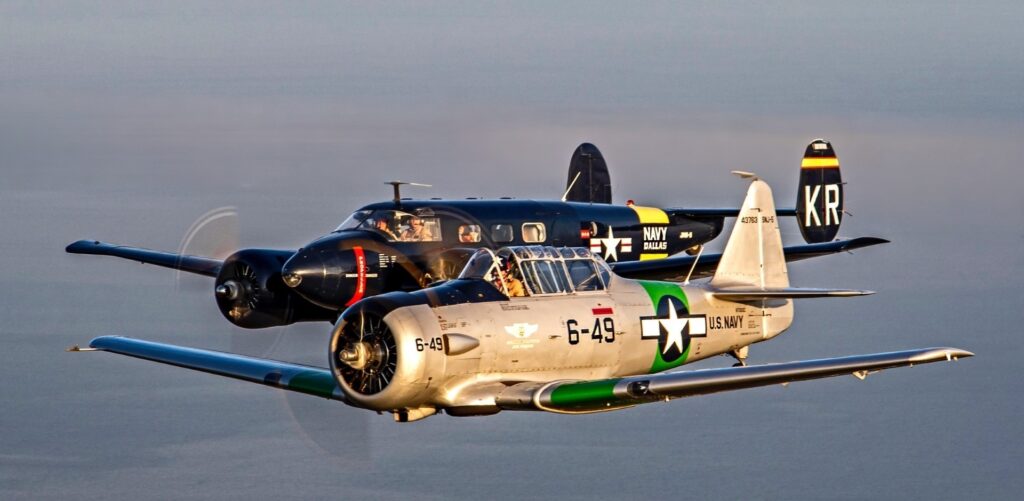 A grey aircraft flies alongside a black aircraft in a formation against a clear sky.